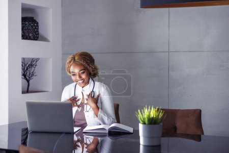 Foto de Médico femenino que tiene una cita de videollamada en línea con el paciente mientras trabaja de forma remota desde la oficina en el hogar, teletrabajo - Imagen libre de derechos