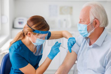 Ein älterer Mann mit medizinischem Mundschutz bekommt im Krankenhaus eine saisonale Grippeimpfung - Impfung, Immunisierung und Krankheitsvorbeugekonzept. Fokus auf den Impfstoff