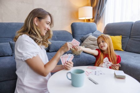 Foto de Hermosa madre e hija pequeña que se divierten pasando tiempo libre juntos en casa jugando a las cartas juego - Imagen libre de derechos