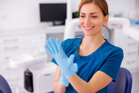 Foto de Médico femenino que se pone guantes quirúrgicos protectores mientras trabaja en el hospital; dentista que se pone guantes médicos de látex antes del procedimiento de cirugía oral - Imagen libre de derechos