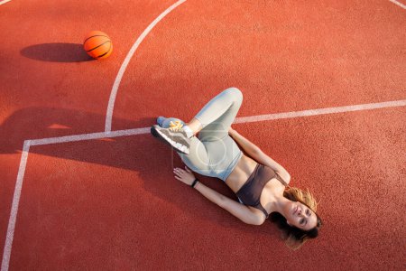 Téléchargez les photos : Vue en angle élevé de la jeune femme active en tenue de sport s'étirant tout en faisant un entraînement en plein air sur un terrain de basket-ball - en image libre de droit