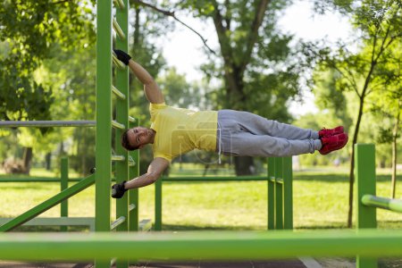 Young athlete working out in an outdoor gym, doing street workout exercises