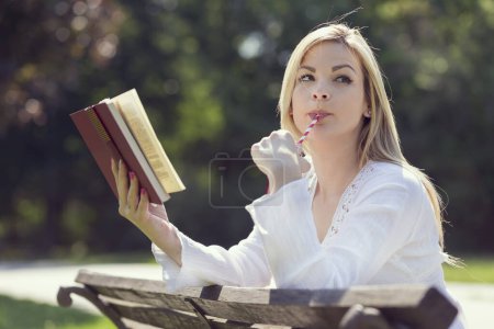 Foto de Retrato de una hermosa joven, bebiendo jugo y leyendo un libro en un día soleado en el parque - Imagen libre de derechos