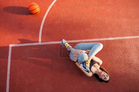 Photo for High angle view of active young woman in sportswear stretching out while doing an outdoor workout on a basketball court - Royalty Free Image