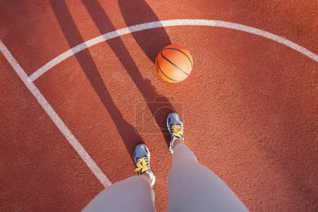 Téléchargez les photos : Ombre vue grand angle de la femme debout sur un terrain de basket-ball en plein air - femme jouant au basket-ball comme routine d'entraînement du matin - en image libre de droit