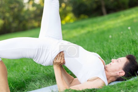 Téléchargez les photos : Femme d'âge moyen faisant du yoga tôt le matin dans un parc - en image libre de droit