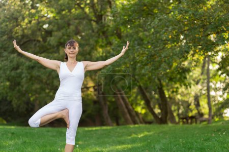 Téléchargez les photos : Femme d'âge moyen faisant du yoga tôt le matin dans un parc - en image libre de droit