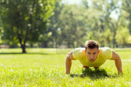 Téléchargez les photos : Un jeune sportif s'entraîne dans un parc, faisant une série de pompes - en image libre de droit