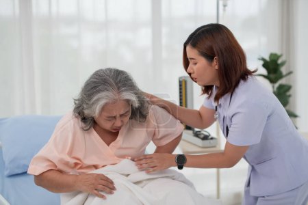 Photo for Asian nurse helping a senior Asian female patient with stomach ache on a bed in hospital ward with diagnosis or treatment, treating elderly woman - Royalty Free Image