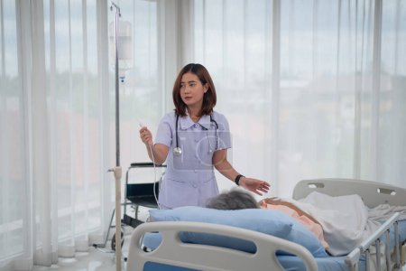 Foto de Enfermera asiática usa bolsa salina de control para paciente mayor en la habitación del hospital, atención médica y médica - Imagen libre de derechos