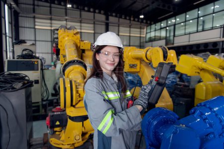 Foto de Ingeniera mujer con casco trabajador de seguridad que trabaja con brazo robótico en fábrica de la industria - Imagen libre de derechos