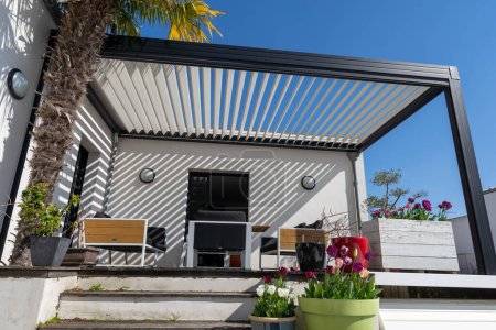 eco friendly structure d'ombre pergola en aluminium bioclimatique, auvent et toit patio, salon de jardin, chaises, barbecue en métal entouré d'aménagement paysager