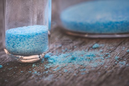 Photo for Blue copper sulphate granules in glass floors - insulated close-up on wood background - Royalty Free Image