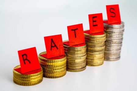 Photo for Stacks of coins, and red bills on top of the word "rates". Increase in interest rates and economic consequences. - Royalty Free Image