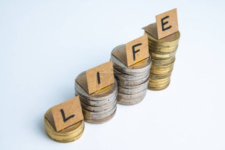 Foto de Montones de monedas, y por encima de los billetes de ortografía de la palabra "vida". Aumento del costo de vida. Aumento de los ingresos. - Imagen libre de derechos