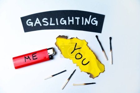 Word Gaslighting, auf einer schwarzen Fläche, neben einem Feuerzeug mit dem Wort Ich und einer verbrannten gelben Karte mit dem Schriftzug Du. Psychologische Bedeutung.