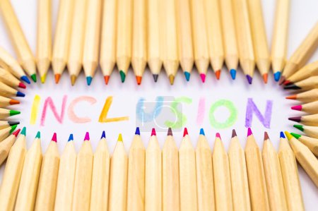 Foto de Colored pencils of different color, next to word "inclusion", written in various colors. Diversity and inclusion. - Imagen libre de derechos