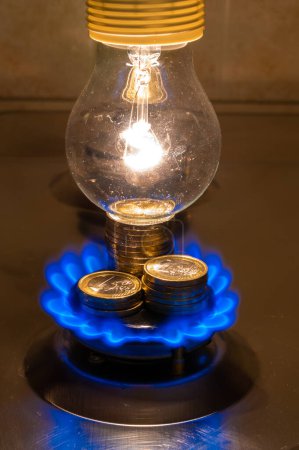 Téléchargez les photos : Light bulb on and lit gas cooker, with coins next to it. Energy and gas costs, cost increases. - en image libre de droit