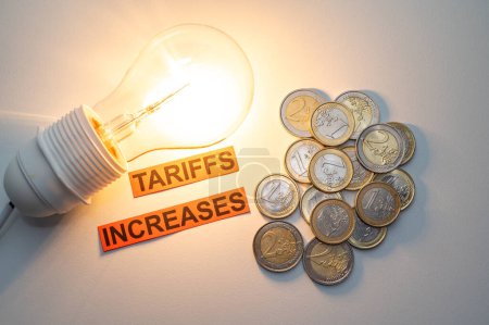 Foto de Lite bombilla, junto a monedas y texto Aumenta las tarifas. Aumento de los costes energéticos. - Imagen libre de derechos