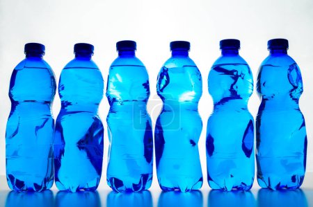 Foto de Frascos transparentes de plástico azul que contienen agua, uno al lado del otro. Uso y reciclado de plástico, protección del medio ambiente. - Imagen libre de derechos