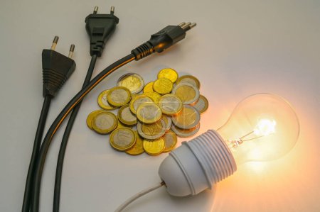 Téléchargez les photos : Ampoule lumineuse, pièces de monnaie, prises électriques. Augmentation et évolution des tarifs énergétiques. - en image libre de droit