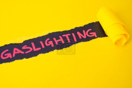 Photo for Black surface, with word gaslighting in red. Underneath torn yellow cardboard. - Royalty Free Image