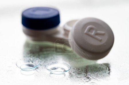 Contact lenses, and case, on mirror surface, with water drops.