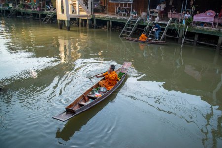 Foto de Un monje budista recoge limosnas y visita hogares en un bote de madera en el Klong Chula del río Mae Klong en la ciudad de Amphawa en la provincia de Samut Songkhram en Tailandia, Tailandia, Amphawa, noviembre de 2022 - Imagen libre de derechos