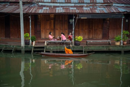 Photo for A  Buddhist monk collect alms and visit households on a woodboat on the Klong Chula of the Mae Klong River in the Town of Amphawa in the Province of Samut Songkhram in Thailand,  Thailand, Amphawa, November, 2022 - Royalty Free Image