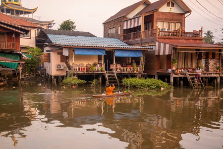 Téléchargez les photos : Un moine bouddhiste recueille l'aumône et visite les ménages sur un bateau à bois sur le Klong Chula de la rivière Mae Klong dans la ville d'Amphawa dans la province de Samut Songkhram en Thaïlande, Thaïlande, Amphawa, Novembre 2022 - en image libre de droit