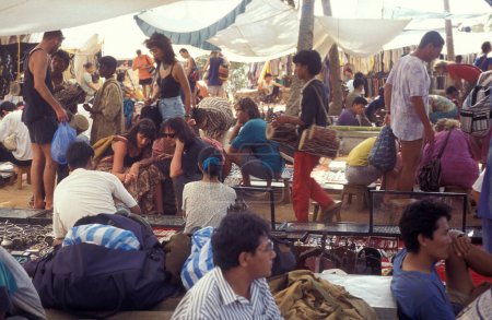Foto de Tiendas y turistas en el antiguo mercado de pulgas de Anjuna en la costa en la ciudad de Anjuna en la provincia de Goa en la India, India, Goa, abril de 1996 - Imagen libre de derechos