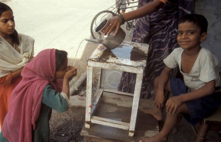 Téléchargez les photos : Une station d'eau publique gratuite d'une famille indienne dans la ville d'Agra dans la province de l'Uttar Pradesh en Inde. Inde, Agra, avril 1998 - en image libre de droit