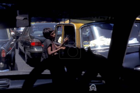 Photo for A Boy begs at a Taxi ta a road in the city centre of Mumbai in India.  India, Mumbai, March, 1998 - Royalty Free Image