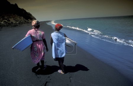Téléchargez les photos : Deux femmes sur la plage de sable noir de lave volcanique à la ville de Sao Filipe sur l'île de Fogo sur les îles du Cap-Vert en Afrique. Cap-Vert, Fogo, mai 2000 - en image libre de droit