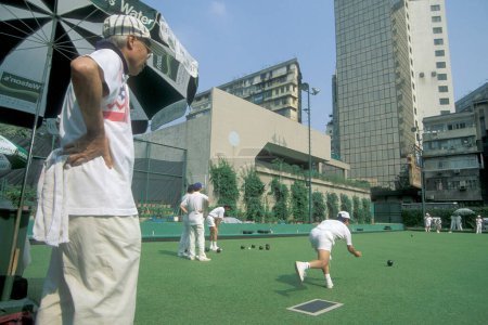 Foto de La gente juega el deporte británico al aire libre Bowling en un green en el centro de Hong Kong en la ciudad de Hong Kong en Hong Kong. China, Hong Kong, junio de 1997 - Imagen libre de derechos