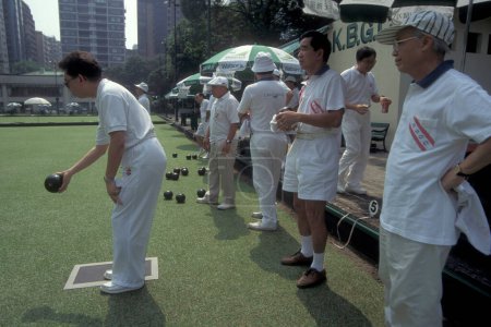 Foto de La gente juega el deporte británico al aire libre Bowling en un green en el centro de Hong Kong en la ciudad de Hong Kong en Hong Kong. China, Hong Kong, junio de 1997 - Imagen libre de derechos