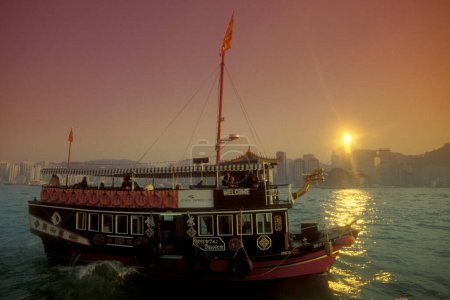 Téléchargez les photos : Un bateau d'excursion lors d'une soirée sur le port de Victoria en face de la Skyline du centre de Hongkong du point de vue de Kowloon dans la ville de Hongkong à Hongkong. Chine, Hongkong, mai 1999 - en image libre de droit