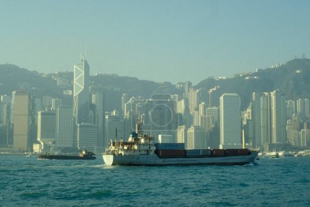 Téléchargez les photos : Un cargo sur le port de Victoria en face du Skyline of Central Hongkong du point de vue de Kowloon dans la ville de Hongkong à Hongkong. Chine, Hongkong, mai 1999 - en image libre de droit