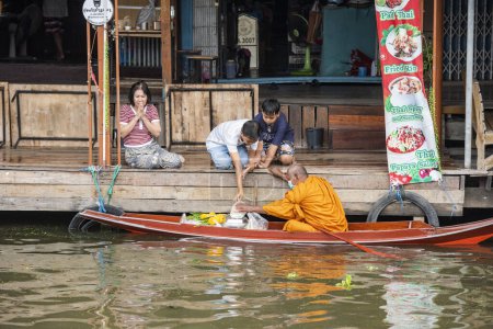 Téléchargez les photos : Un moine bouddhiste sur son aumône matinal donnant une visite sur un bateau à bois à la rivière Damnoen Saduak et un marché flottant dans la province de Ratchaburi en Thaïlande, Thaïlande, Ratchaburi, 12 novembre 2023 - en image libre de droit
