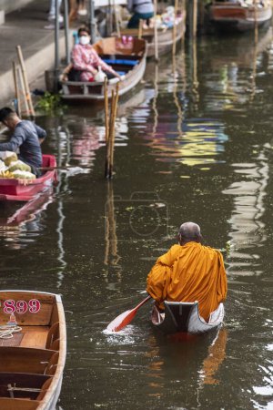 Téléchargez les photos : Un moine bouddhiste sur son aumône matinal donnant une visite sur un bateau à bois à la rivière Damnoen Saduak et un marché flottant dans la province de Ratchaburi en Thaïlande, Thaïlande, Ratchaburi, 12 novembre 2023 - en image libre de droit