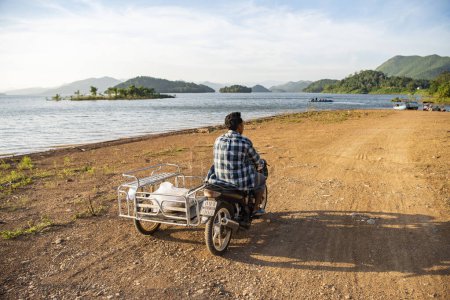 Photo for Thailand, Phetchaburi - November 19, 2023: Motorbike driver at the Lake Kaeng Krachan Dam in the Kaeng Krachan National Park in the Province of Phetchaburi in Thailand. - Royalty Free Image
