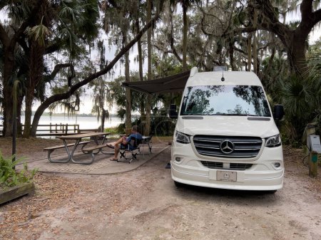 Téléchargez les photos : Mount Dora, FL États-Unis - 13 décembre 2022 : Un homme par un véhicule récréatif assis au bord du lac à Trimble Park à Mount Dora, Floride par une journée ensoleillée d'hiver. - en image libre de droit
