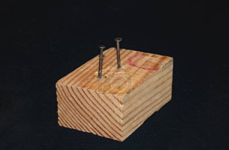 Téléchargez les photos : Un bloc de bois avec deux clous vissés. Fond noir - en image libre de droit