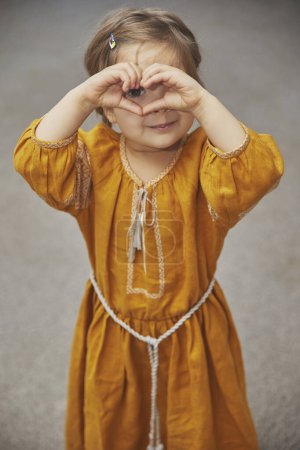 Téléchargez les photos : Belle enfant en robe brodée ukrainienne montrant coeur avec les mains - en image libre de droit