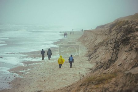 Photo for People walk on the beach in stormy weather in Sondervig Denmark. - Royalty Free Image