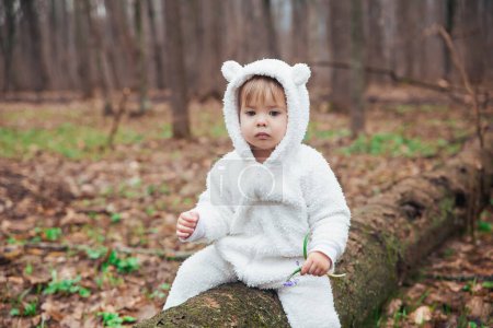Liebenswertes Baby im Bärenkostüm im Wald an einem umgestürzten Baum.
