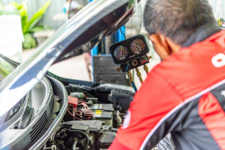 Photo for Bangkok, Thailand - May 4, 2023 : Unidentified car mechanic or serviceman refilling air condition and checking a air compressor for fix and repair problem at car garage or repair shop - Royalty Free Image