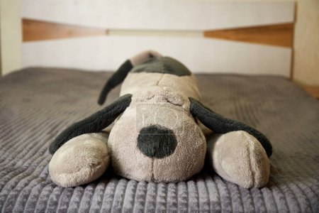 Un jouet farci pour chien sur le lit sur un couvre-lit gris.