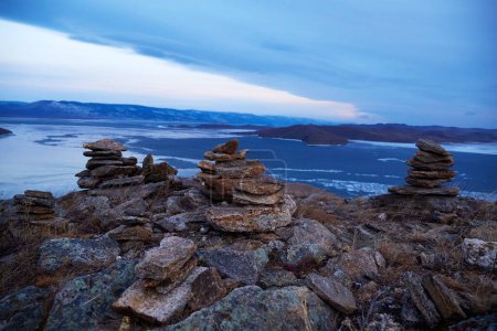 Pyramids of stones built by tourists on an open mountainside. Beautiful view of Lake Baikal in winter at dawn. The concept of travel, hiking and outdoor activities