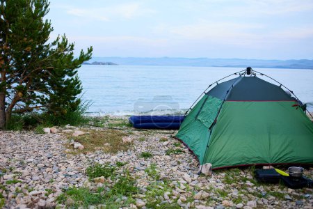 Une tente sur une plage de galets au bord du lac à l'aube. Un endroit pour camper.